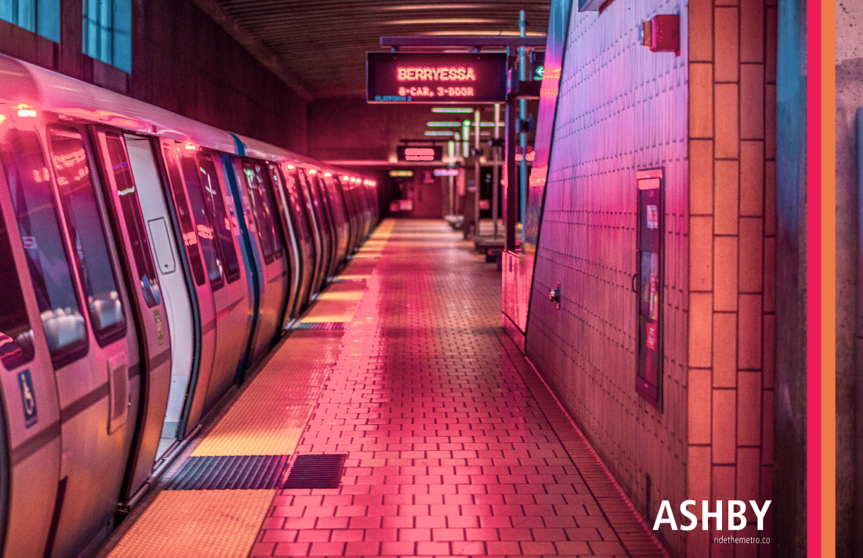 A photo poster design that says Ashby, with orange and red vertical lines overlaid. The photo is of a fleet of the future train at the Ashby station platform, an indoor brick station with some windows, with dusky pink lighting, looking parallel with the train along the platform.